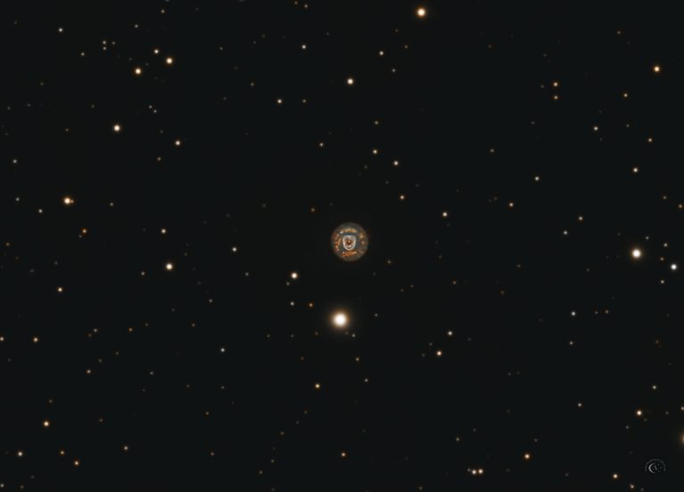 Astrofotografie von NGC 2392 im Sternbild Zwillinge: kompakter planetarischer Nebel mit heller blaugrüner Innenregion, orangefarben betonter Außenschale und feinen radialen Strukturen im dichten Sternfeld.